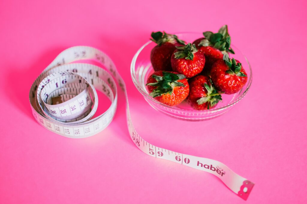 Holistic Weight Loss A glass bowl of fresh strawberries paired with a pink measuring tape symbolizes healthy eating.