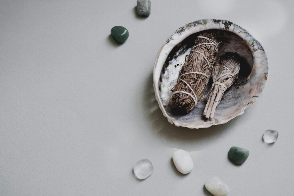 Flat lay of sage bundles and gemstones in an abalone shell for spiritual rituals.